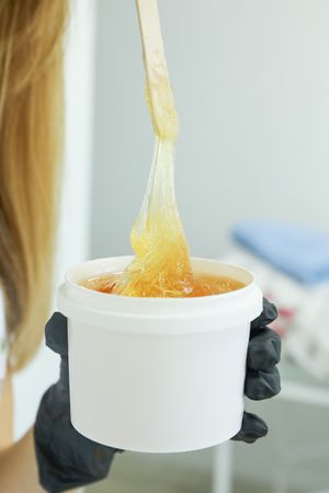 Woman holding liquid yellow paste for sugaring, close up