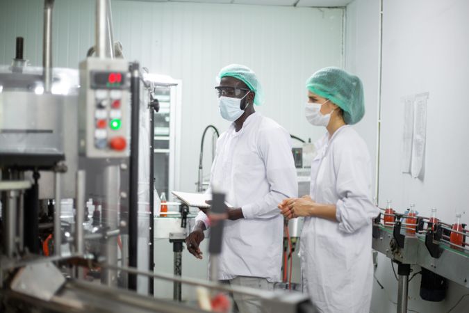 Two diverse factory workers are inspecting machinery inside a beverage production facility.