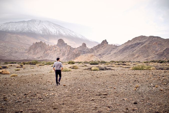 Unrecognizable male traveler walking on rocky terrain near hills