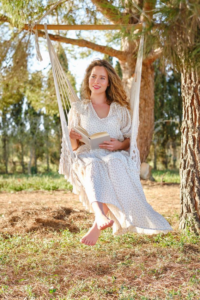 Happy female with book resting on hammock on tree branch