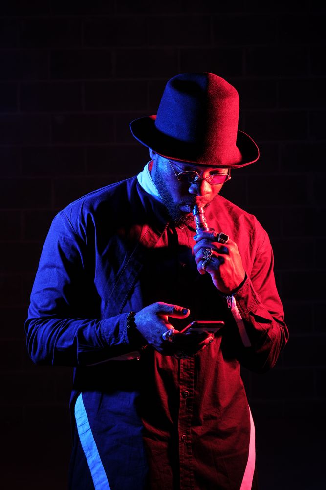 Stylish Black man vaping and browsing smartphone