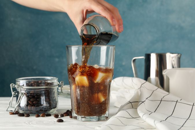 Woman pours a glass of coffee. Composition with ice coffee