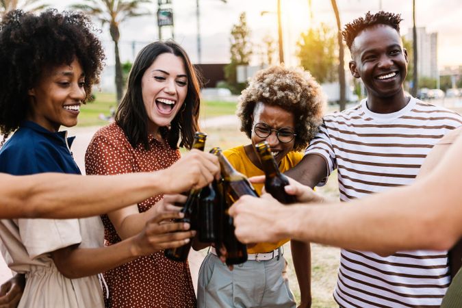 Happy young multiracial friends celebrating and cheering with beer at summer party outdoors