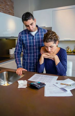 Worried couple going through their bills together in the kitchen, vertical