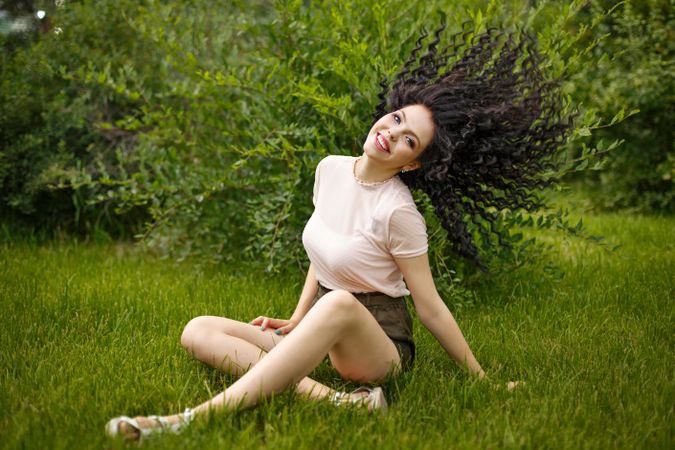Teenage girl flicking her dark curly hair while sitting in the grass