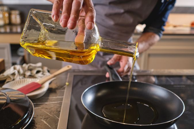 Unrecognizable man pouring oil into frying pan