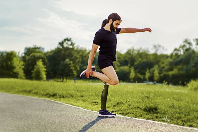 Athletic man with disability - a prosthetic leg - stretching before his workout outdoors in the park
