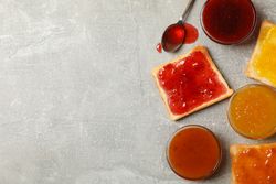 Bowls and toasts with jam on gray background, top view