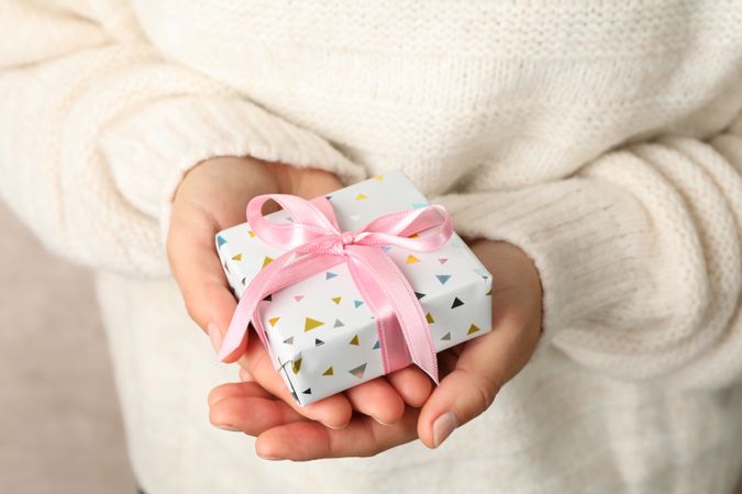 Woman in sweater holding gift box with pink bow, close up