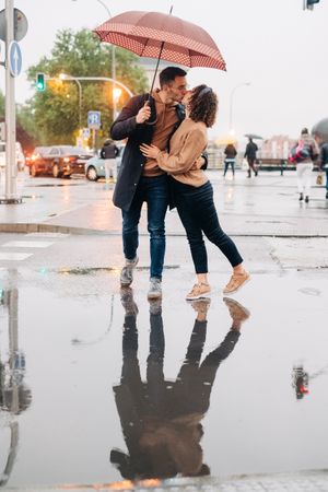 Happy couple with umbrella hugging on wet street