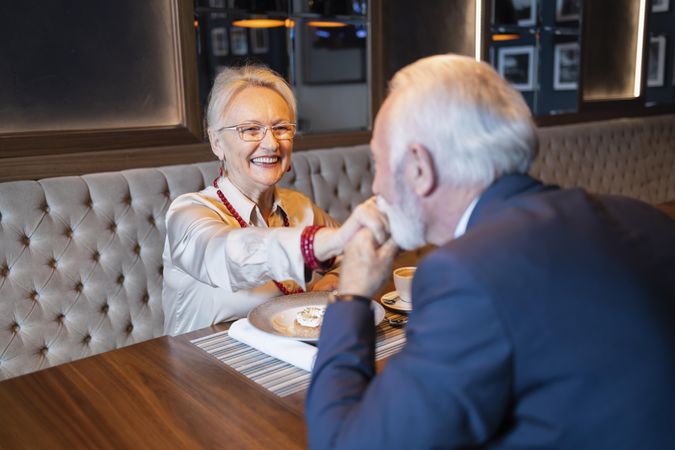 Older man kissing hand of happy woman on dinner date