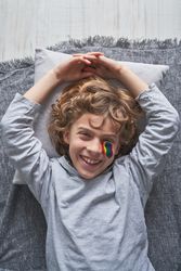 Cheerful boy with rainbow drawing lying on pillow