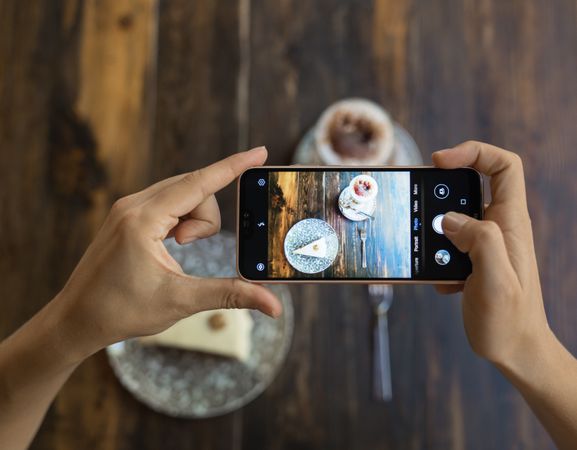 Faceless person taking picture of cake and coffee