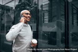 Smiling man walking to office carrying office bag and talking over phone 0gwo80