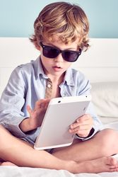 Barefoot boy in sunglasses using tablet on bed