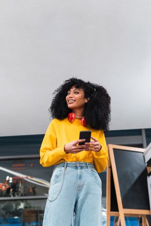 Cheerful stylish female standing and using smartphone in contemporary building