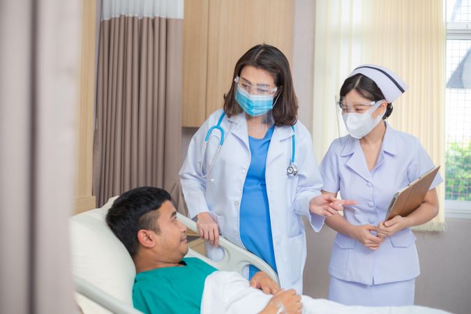 Two female medical professionals treating male in hospital bed