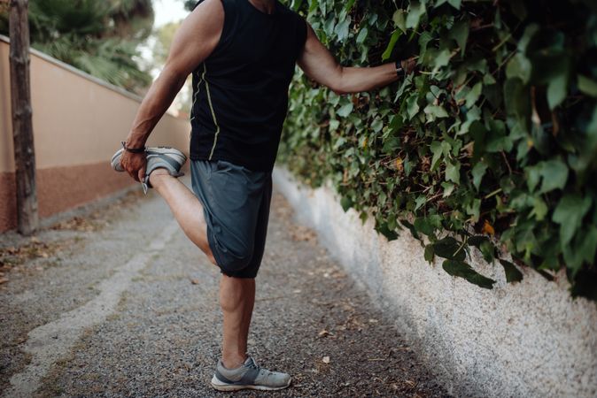 Older man stretching leg holding botanical wall in street
