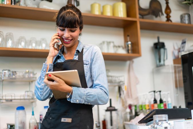 Woman speaking on phone working in cafe with digital tablet in hand