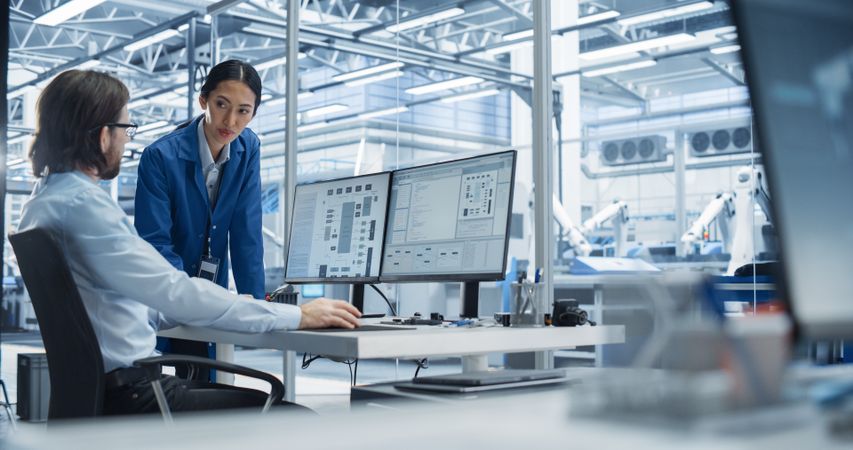 Portrait of a Young Male Engineer and a Asian Team Leader Collaborating on a Project, Using Computer and Talking in a Factory with Equipment Producing Modern Technical Devices for Tech Industries