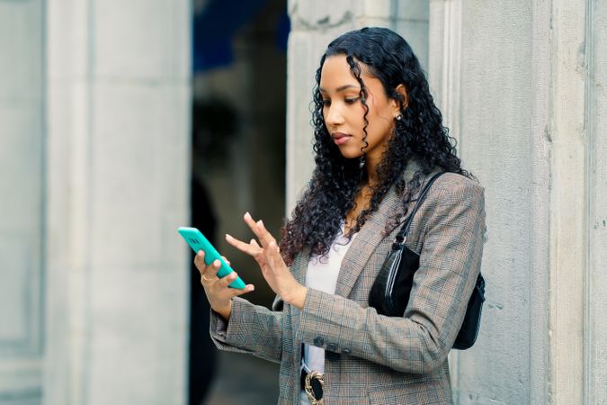 A stylish young woman engages with her smartphone in an urban setting, showcasing her beauty