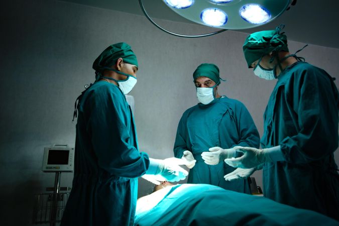 Three medical professionals in scrubs standing over a patient in hospital