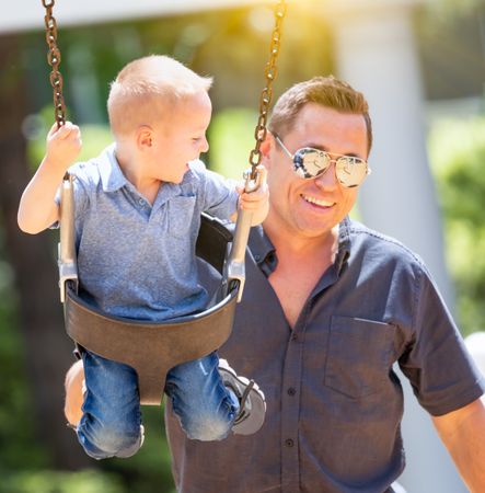 Happy Young Boy Having Fun On The Swings With His Father At The Playground