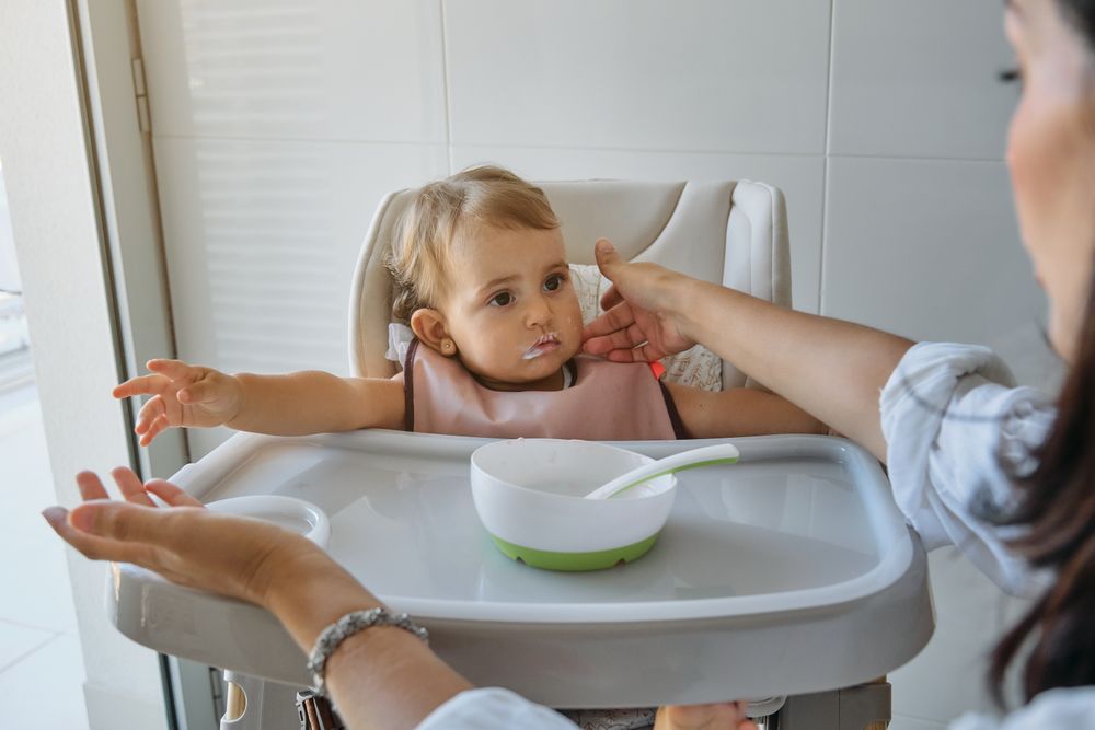 Baby girl sitting on high chair and looking at mother