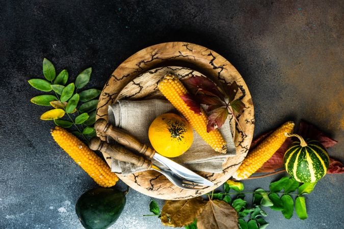 Top view of rustic Thanksgiving table setting with squash and corn on brown tableware