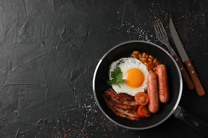 Top view of breakfast in pan with eggs, tomatoes, sausage and bacon, copy space