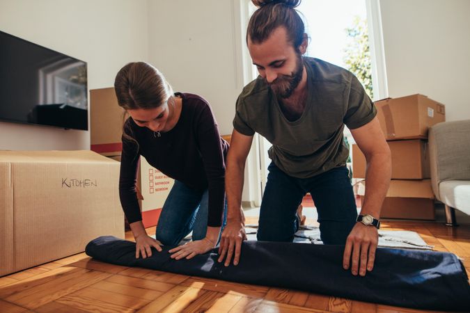 Couple working together to roll up a carpet on floor for packing