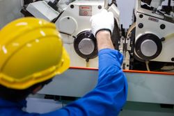 Male in blue jumpsuit and PPE gear operating controller in manufacturing plant