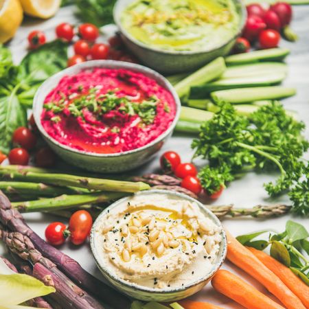 Fresh colorful vegetables and dips with hummus, avocados, asparagus, carrots, square crop, close up