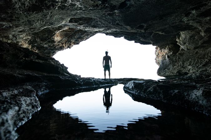 Silhouette of man standing beside river and cave