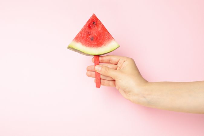 Female hand holds watermelon slice on pink background. Summer fruit