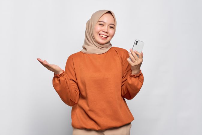 Open Muslim woman holding smart phone and palm up questioning