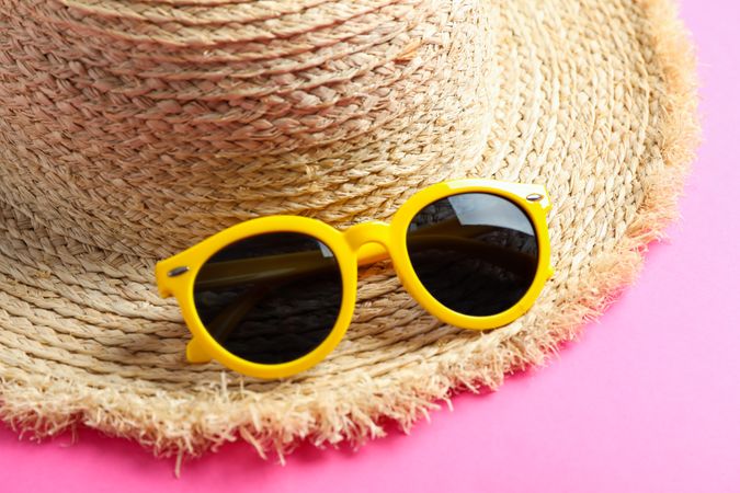 Straw hat with sunglasses on color background, closeup. Summer backdrop