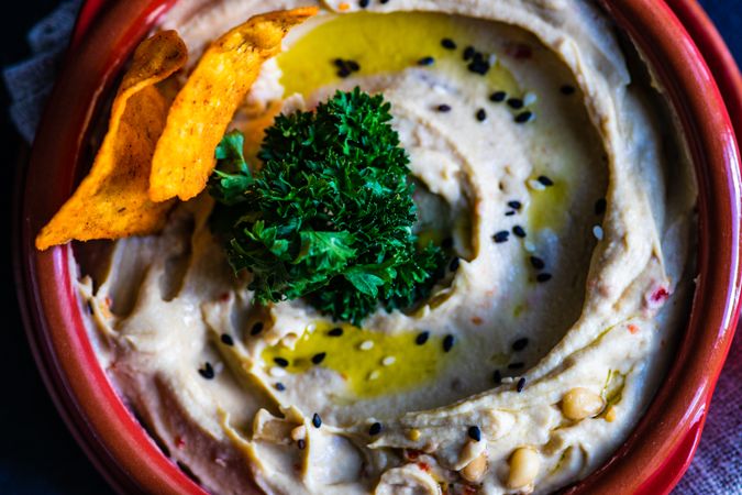 Close up top view of creamy hummus dip with olive oil, garnish and chips