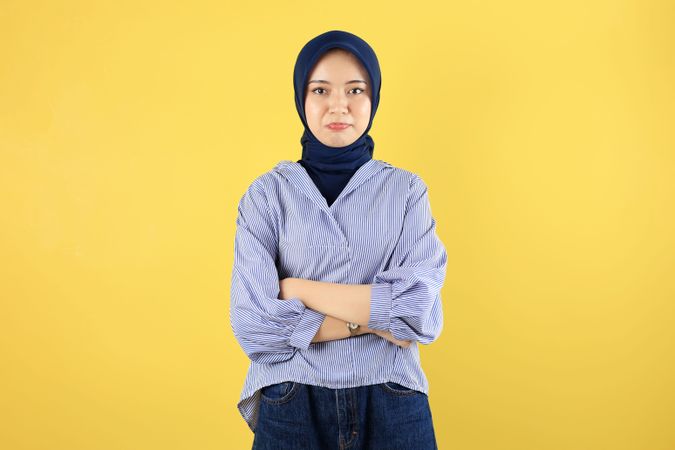 Displeased Young Asian Woman in Blue Striped Blouse and Navy Hijab Standing with Arms Crossed