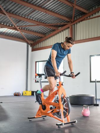 Sportsman exercising on stationary bicycle in light modern gym