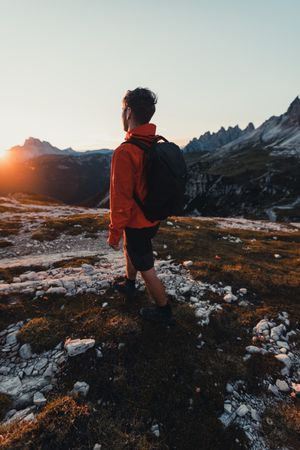Back view of man in red jacket with backpack hiking in the mountains at sunset