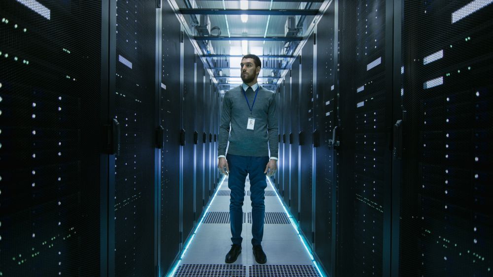 Curios IT Engineer Standing in the Middle of a Working Data Center Server Room.