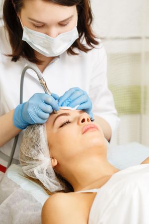 Woman having beauty treatment with machine on her forehead, vertical