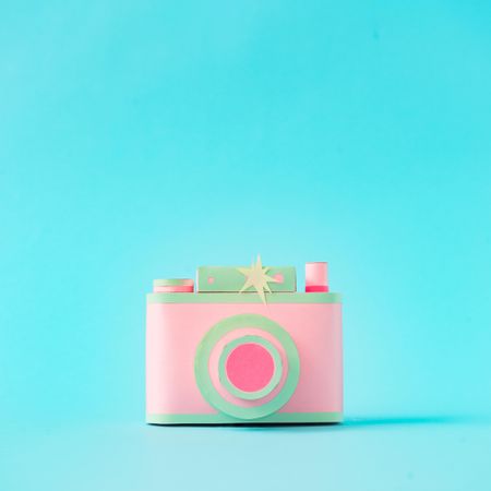 Vintage camera made of pink and green paper on bright blue background