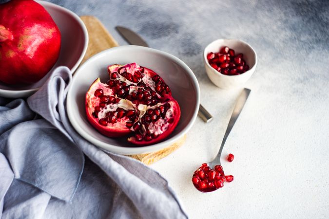 Fresh cut pomegranate in light bowl, with spoon of seeds