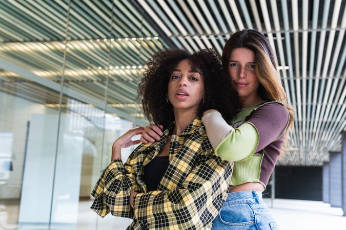 Young multiethnic girlfriends embracing against glass wall