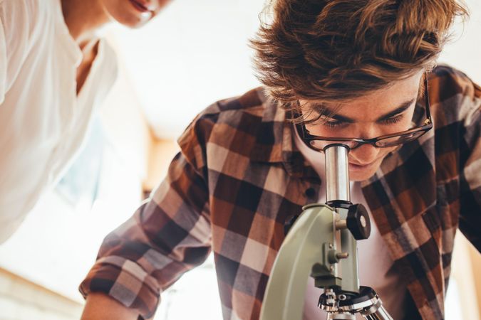 Male student looking at slides through a microscope in class