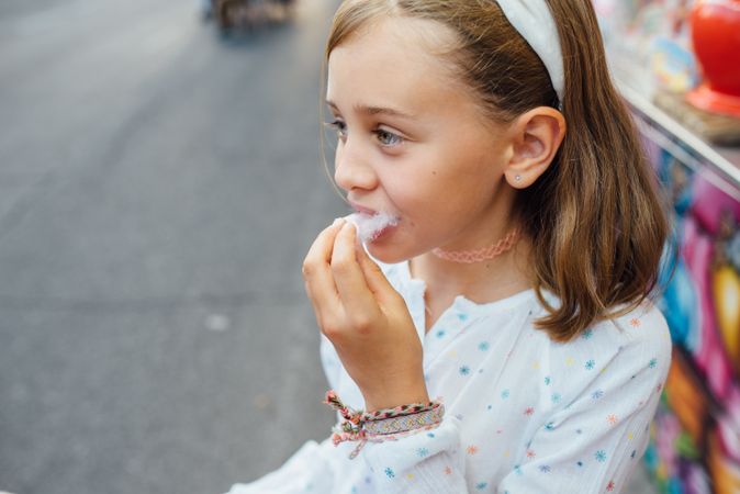 Cheerful girl eating cotton candy on street