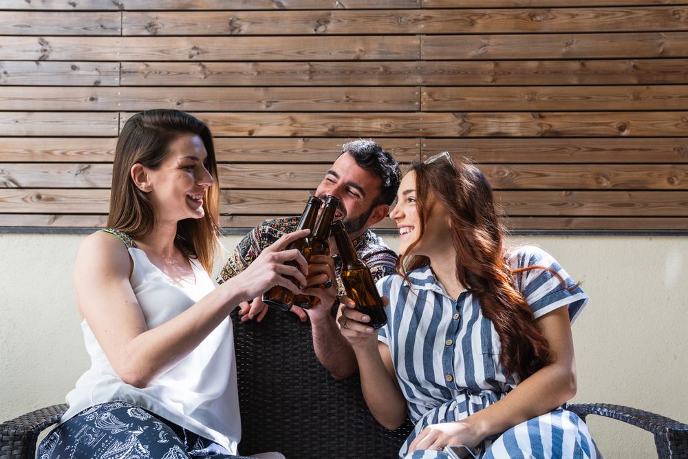 Cheerful friends with beer spending weekend on sofa