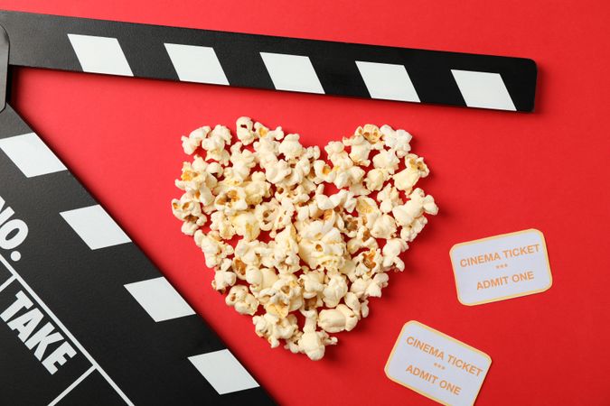 Heart laid out from popcorn, clapperboard and tickets on red background, top view